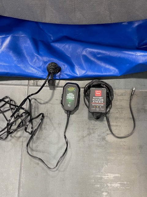 Two 12V battery maintainers — a Battery Tender Junior and a Battery Manager Junior II — plugged into the FloodVault charger port on the blue vault.