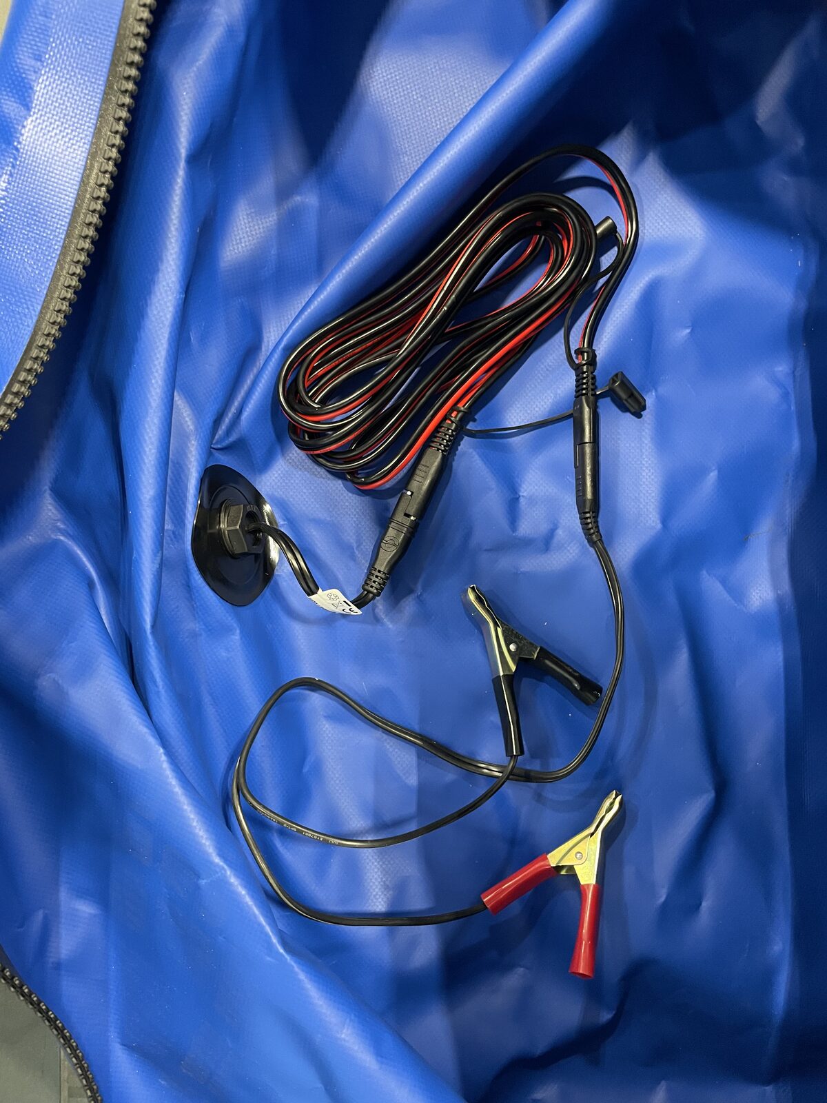 Inside the FloodVault: the SAE charger lead with ring terminals and alligator clips coiled next to the interior side of the sealed pass-through port.